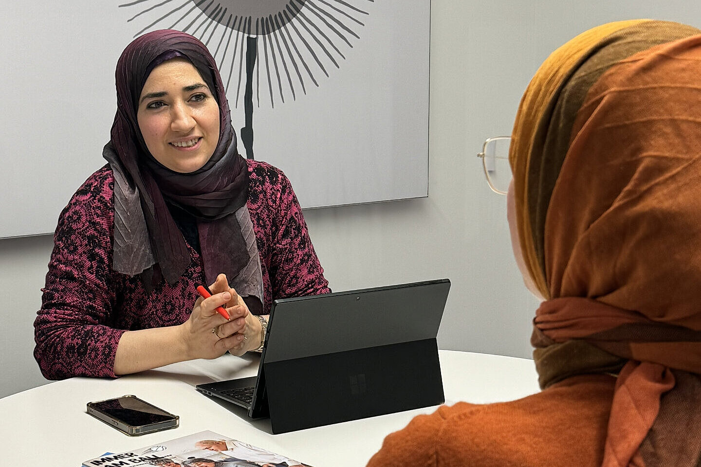 Eine Frau mit Hijab sitzt mit einem Laptop an einem Tisch und sucht Migrations- und Integrationsberatung bei der AWO Mönchengladbach.